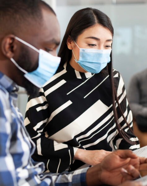 Diverse candidates wait in office lobby Closeup of asian woman reading application form of black man, both seated in office lobby waiting for interview meeting. Multiethnic male and female job candidates with face masks, sharing ideas.